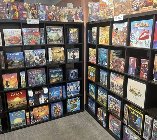 Shelves filled with a variety of colorful board games, each with unique artwork. The scene exudes a lively and inviting hobby shop.